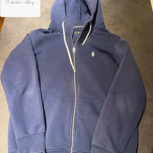 Blå hoodie från Ralph Lauren - Säljer en snygg blå hoodie från Ralph Lauren med dragkedja och huva. Den har en liten broderad logga på bröstet och ribbade muddar vid ärmslut och nederkant. Perfekt för en avslappnad stil. Riktigt bra skick 9/10 storlek L passar M-L