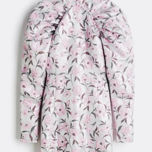 Blommig klänning med puffärmar - Elegant klänning med ett vackert blommönster i rosa och grått. Klänningen har långa puffärmar och en hög hals med knappar som detalj. Perfekt för en stilfull look.