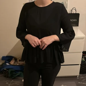 Svart mesh blus från Monki - Snygg svart volangblus från Monki med v-ringning och vida trekvartsärmar. Perfekt för en stilren look.