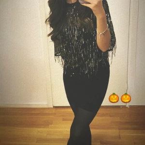 Svart blus med paljetter - Snygg svart tröja med glittriga paljetter som ger en festlig look. Tröjan har korta ärmar och en figurnära passform som framhäver silhuetten. Perfekt för en utekväll eller festlig tillställning. Använd endast 1 gång. 