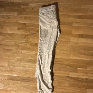 Beige byxor från Knowledge Cotton Apparel - Snygga beige byxor från Knowledge Cotton Apparel. De har en klassisk design med normal passform och är tillverkade i bomull. Perfekta för en stilren look.