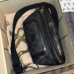 Svart midjeväska från Gucci - Snygg svart midjeväska från Gucci med klassiskt mönster och dragkedja. Perfekt för att bära dina nödvändigheter med stil. Justerbar rem för bekväm passform.  Pris kan diskuteras. Finns kvitto också.