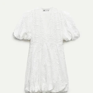 Vit klänning från Zara - Vit klänning från Zara med puffiga kortärmar och v-ringad design. Klänningen har ett vackert blommigt mönster och en luftig passform. Klänningen var som en ”ballong” nedtill, men som man ser på bild två så ändrade jag det till bara rakt för att den skulle bli lite längre. 