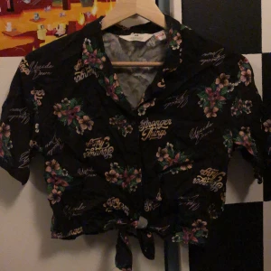 Svart Stranger Things skjorta från H&M - svart skjorta från H&M med Stranger Things-tryck och blommönster. Skjortan har blomtryck och går även att knyta på framsidan. Har bara använts 2-3 gånger