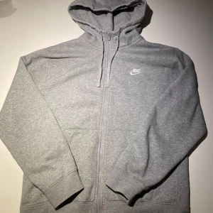 Grå hoodie från Nike - Säljer en klassisk grå hoodie från Nike med dragkedja och huva. Perfekt för en avslappnad stil. Den har långa ärmar och en liten Nike-logga på bröstet. Bra skick, passar både M och L