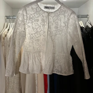 Vit broderad jacka från Zara - Elegant vit jacka från Zara med vackra broderade blommor och pärldetaljer. Jackan har en rund halsringning och långa ärmar, perfekt för en stilren look. Storlek L