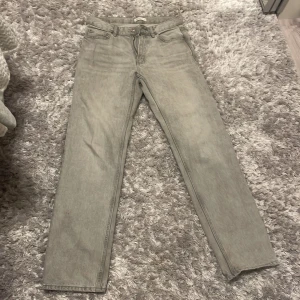 Grå jeansbyxor - Snygga grå jeansbyxor med klassisk femficksdesign och rak passform. Perfekta för en avslappnad stil. De har en dragkedja och knapp framtill.