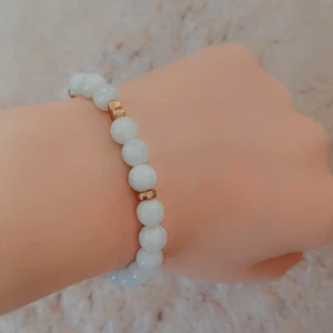 Armband  - Elegant armband med vita pärlor och guldfärgade detaljer. Perfekt för att ge en stilren touch till din outfit. Elastiskt band för enkel passform.