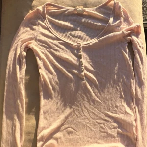 Ljusrosa ribbad tröja från H&M - Säljer en ljusrosa ribbad tröja från H&M med rund hals och knappar framtill. Tröjan har långa ärmar och är perfekt för en avslappnad stil. Passar bra till både jeans och kjol.