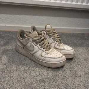 Vita Nike Air Force sneakers - Säljer ett par klassiska vita Nike Air Force sneakers. De har en ikonisk design med snörning och Nike-logga på sidan. Perfekta för en avslappnad stil.