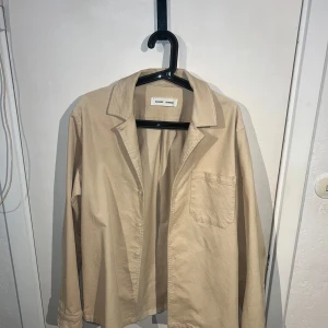 Beige overshirt från Samsøe Samsøe - Snygg beige overshirt från Samsøe Samsøe i en stilren design. Perfekt för lager-på-lager looken. Den har en klassisk krage och en bröstficka som ger en avslappnad stil. Passar perfekt för vår och höst. Nypris 1699:-