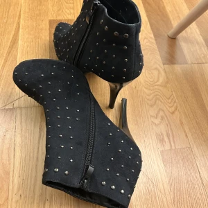 Svarta boots med nitar - Snygga svarta boots med hög klack och dragkedja på sidan. Skorna är dekorerade med små nitar över hela ytan, vilket ger dem en tuff och stilren look. Perfekta för att ge din outfit en extra edge.