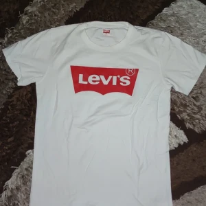Vit t-shirt från Levi's - Klassisk vit t-shirt från Levi's med det ikoniska röda logotyptrycket på bröstet. Perfekt för en avslappnad stil.
