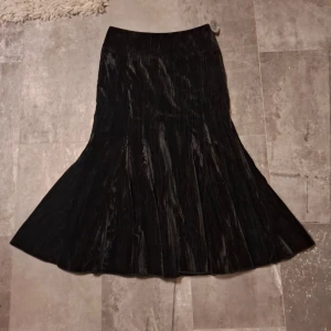 Svart långkjol från Prêt à Porter - Elegant svart långkjol från Prêt à Porter i ett glansigt material som ger en lyxig känsla. Kjolen har en vacker fall och är perfekt för speciella tillfällen. Den är i storlek 36 och har en klassisk design som passar många stilar.