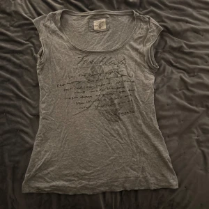 Grå ärmlös topp från L.O.G.G. - Säljer en grå ärmlös topp från L.O.G.G. med tryck på framsidan. Perfekt för en avslappnad stil. Tillverkad i Turkiet.