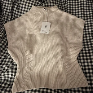 Beige stickad topp från & Other Stories - Säljer en stilren beige stickad topp från & Other Stories. Toppen har en hög krage och är ärmlös, perfekt för lager-på-lager under kyligare dagar. Den är tillverkad i ull vilket gör den både varm och bekväm. Toppen är aldrig använd och är i mycket fint skick🫶🏼