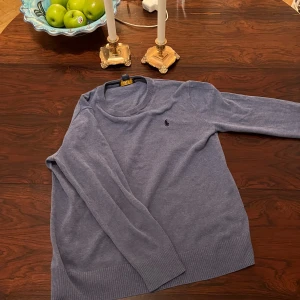 Blå tröja från Ralph Lauren - Säljer en stilren blå tröja från Ralph Lauren i 100% bomull. Tröjan har en broderad logotyp på bröstet och ribbade kanter vid ärmslut och nederkant. Perfekt för en avslappnad och snygg look. Tröjan har krymt och skulle säga att den passar 150-160 cm,11/12 år