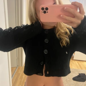 Svart kofta med fransdetaljer - Snygg svart kofta med knappar och unika fransdetaljer längs ärmarna. Den är croppad och har en snygg design som passar perfekt för att ge en extra touch till din outfit. Perfekt att ha över linne eller klänning i sommar eller ba t-shirt. Så unik. Köpt vintage i CPH 💗inga defekter (ba spegeln som e smutsig haha)