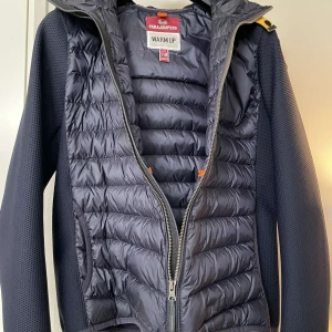 Mörkblå jacka från Parajumpers - jacka med huva från Parajumpers. Jackan är vadderad på bröst och rygg och ärmarna är i ett meshmaterial. Jackan har sidofickor, bröstficka och bakficka som stängs med   dragkedja. Denna jacka är perfekt att ha som den är under höst, vår och sommar. Köpt för 3800kr från kidsbrandstore