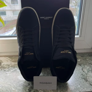 Svarta sneakers från Saint Laurent - Snygga svarta sneakers från Saint Laurent med vit sula och märkets logga i vitt på sidan. Skorna har klassisk snörning och en stilren design som passar perfekt för en trendig look.