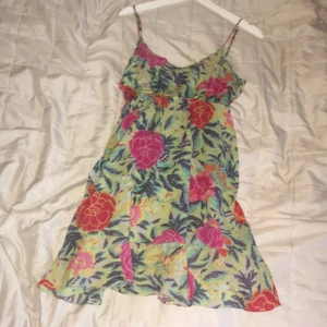Blommig sommarklänning med smala axelband - Säljer en färgglad sommarklänning med blommigt mönster i rosa, rött och grönt. Klänningen har smala axelband och en luftig passform, perfekt för varma dagar. Den är tillverkad i ett lätt och bekvämt material, och väldigt vacker att ha när man åker utomlands som tillexempel, Spanien, mauritsius eller liknande, tror jag köpte på en marknad utomlands, priset då låg rund 299kr