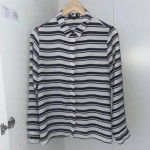 Svartvit randig skjorta - Snygg svartvit randig skjorta med långa ärmar och knappar framtill. Perfekt för en stilren look. Skjortan har en klassisk krage och är tillverkad i ett lätt material.