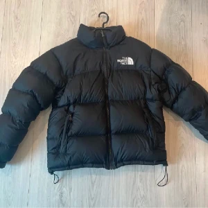 The North Face jacka - Säljer en svart dunjacka från The North Face. Jackan har en pufferdesign med dragkedja och hög krage för extra värme. Perfekt för kyliga dagar. Skick 9/10, köpt från ASOS. Nypris 3799kr