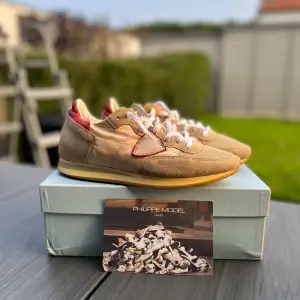 Säljer ett par snygga beige sneakers från Philippe Model. De har en stilren design med mockadetaljer och en röd accent på hälen. Skorna har vita snören och en bekväm gummisula. Perfekta för både vardag och fest Pris kan även diskuteras vid snabbt köp