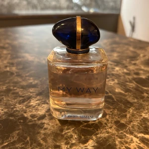 My Way parfym från Giorgio Armani - Elegant parfymflaska från Giorgio Armani med namnet 'My Way'. Flaskan är genomskinlig med en stilren design och har en djupblå, oval kork med gulddetaljer. Perfekt för den som söker en sofistikerad doftupplevelse.