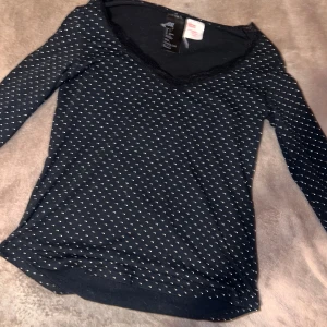 Svart prickig tröja - Snygg svart topp från H&M med vita prickar och spetsdetaljer vid v-ringningen. Perfekt för en stilren look. Långärmad och tillverkad i ett mjukt material för extra komfort.