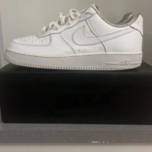 Vita Nike Air Force sneakers - Klassiska vita Nike Air Force sneakers med snörning och perforerade detaljer på tån. Dessa sneakers har en ikonisk design med en robust sula och är perfekta för en stilren look.