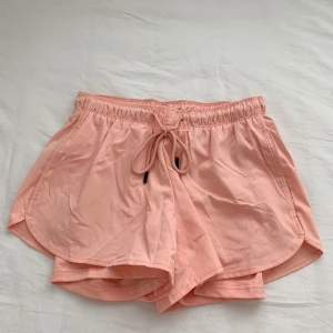 Rosa shorts med snörning - Snygga och bekväma rosa shorts med elastisk midja och snörning framtill. Perfekta för varma sommardagar eller träning. De har en lös passform som ger en avslappnad stil.