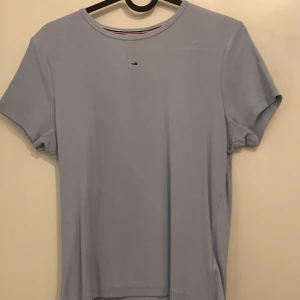 Ljusblå t-shirt från Tommy Hilfiger - Snygg ljusblå t-shirt från Tommy Hilfiger med en liten logga på bröstet. Perfekt för en avslappnad stil. Tillverkad i mjukt material för extra komfort.