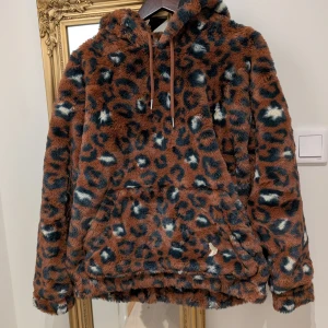Leopardmönstrad hoodie från ASOS DESIGN - Säljer en fluffig och trendig leopardmönstrad hoodie från ASOS DESIGN. Den har en mysig huva och en stor ficka framtill. Perfekt för att hålla sig varm och stilren under kyliga dagar.