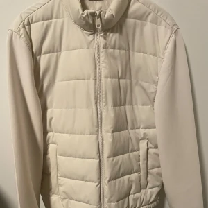 Beige quiltad jacka från Zara - Säljer en stilren beige quiltad jacka från Zara. Jackan har en dragkedja framtill och långa ärmar. Perfekt för kyligare dagar med sin mjuka och bekväma passform. Fint skick och knappt använd storlek:M men passar även S