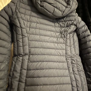 Svart dunjacka från Parajumpers - Säljer en svart dunjacka från Parajumpers i superlätt material. Jackan har en lång passform med dragkedja framtill och långa ärmar. Perfekt för kyliga dagar.