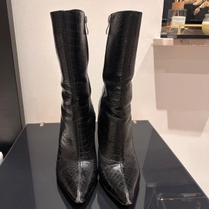 Svarta stövletter med krokodilmönster - Snygga svarta stövletter med krokodilmönster och spetsig tå. De har en dragkedja på sidan för enkel på- och avtagning samt en stabil klack för extra höjd.