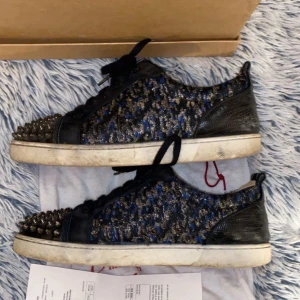 Christian Louboutin  - Snygga Christian Louboutin sneakers med svarta och blå detaljer samt nitar på tån. Skorna har en unik design med glittrigt mönster och snörning. Perfekta för att sticka ut i mängden. Box och kvitto finns, hör av er vid frågor!