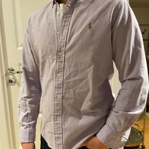 Ljuslila skjorta från Ralph Lauren - Snygg ljuslila skjorta från Ralph Lauren i slim fit. Skjortan har långa ärmar och knappar framtill. Perfekt för en stilren look.