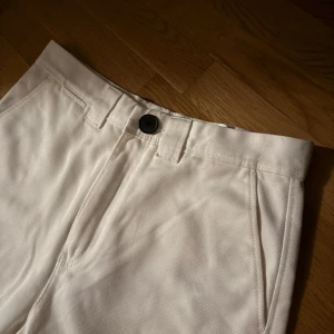 Benvita byxor från Weekday - Snygga benvita byxor från Weekday med en klassisk design. De har en knapp och dragkedja framtill samt fickor både fram och bak. Perfekta för en stilren look.