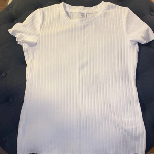 Vit ribbad t-shirt från Lindex - Säljer en vit ribbad t-shirt från Lindex i storlek 146/152. T-shirten har korta ärmar och en klassisk rund halsringning. 