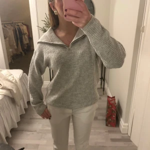 Grå ribbad tröja med dragkedja - Säljer en stilren grå ribbad tröja med dragkedja och stor krage. Perfekt för kyligare dagar. Tröjan har långa ärmar och en avslappnad passform.