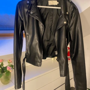 Svart skinnjacka från H&M - Snygg svart skinnjacka från Nelly  med dragkedja och knappar. Perfekt för en cool och edgy look.