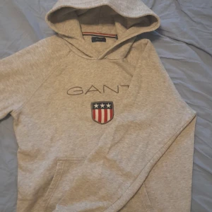 Grå hoodie från GANT - Säljer en stilren grå hoodie från GANT. Tröjan har en klassisk luva och en praktisk magficka. Passar dig mellan 150-163cm