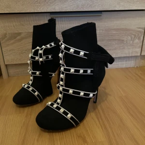 Svarta klackskor från Valentino - Snygga svarta klackskor från Valentino med vita nitar och remmar. Perfekta för att ge en edgy touch till din outfit. Skorna har en spetsig tå och hög klack.