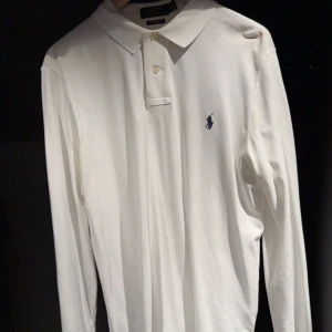 Vit pikétröja från Ralph Lauren - Säljer en klassisk vit pikétröja från Ralph Lauren i custom slim fit. Tröjan har långa ärmar och en broderad logotyp på bröstet. Perfekt för en stilren look.