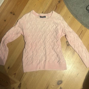 Ljusrosa stickad tröja från Pahladium - Mysig ljusrosa stickad tröja från Pahladium med ett diskret mönster. Tröjan har långa ärmar och ribbade kanter vid hals och ärmslut. Perfekt för kyligare dagar!