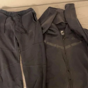 Svart hoodie från Nike - Säljer en svart hoodie från Nike med dragkedja och huva. Perfekt för en avslappnad stil. Den har långa ärmar och en klassisk design med Nike-loggan diskret på bröstet.