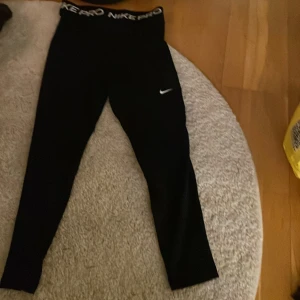 Svarta leggings från Nike Pro - Säljer ett par svarta Nike Pro leggings med hög midja och elastisk linning. Perfekta för träning med en tight passform och Nike-logga på benet. Klippt av prislappen men dom är köpa på stadium!