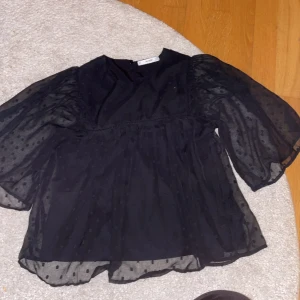 Svart blus från Mango - Snygg svart blus från Mango med transparenta puffärmar och prickigt mönster. Blusen har en lös passform och rund halsringning, perfekt för en stilren look.